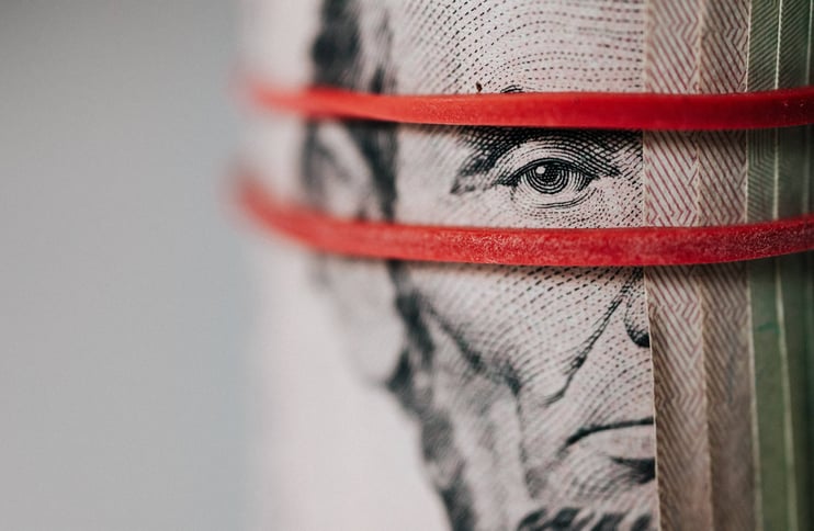 A roll of $5 bills, wrapped by a red rubber band. Lincoln's eye peers through a gap in the bands.